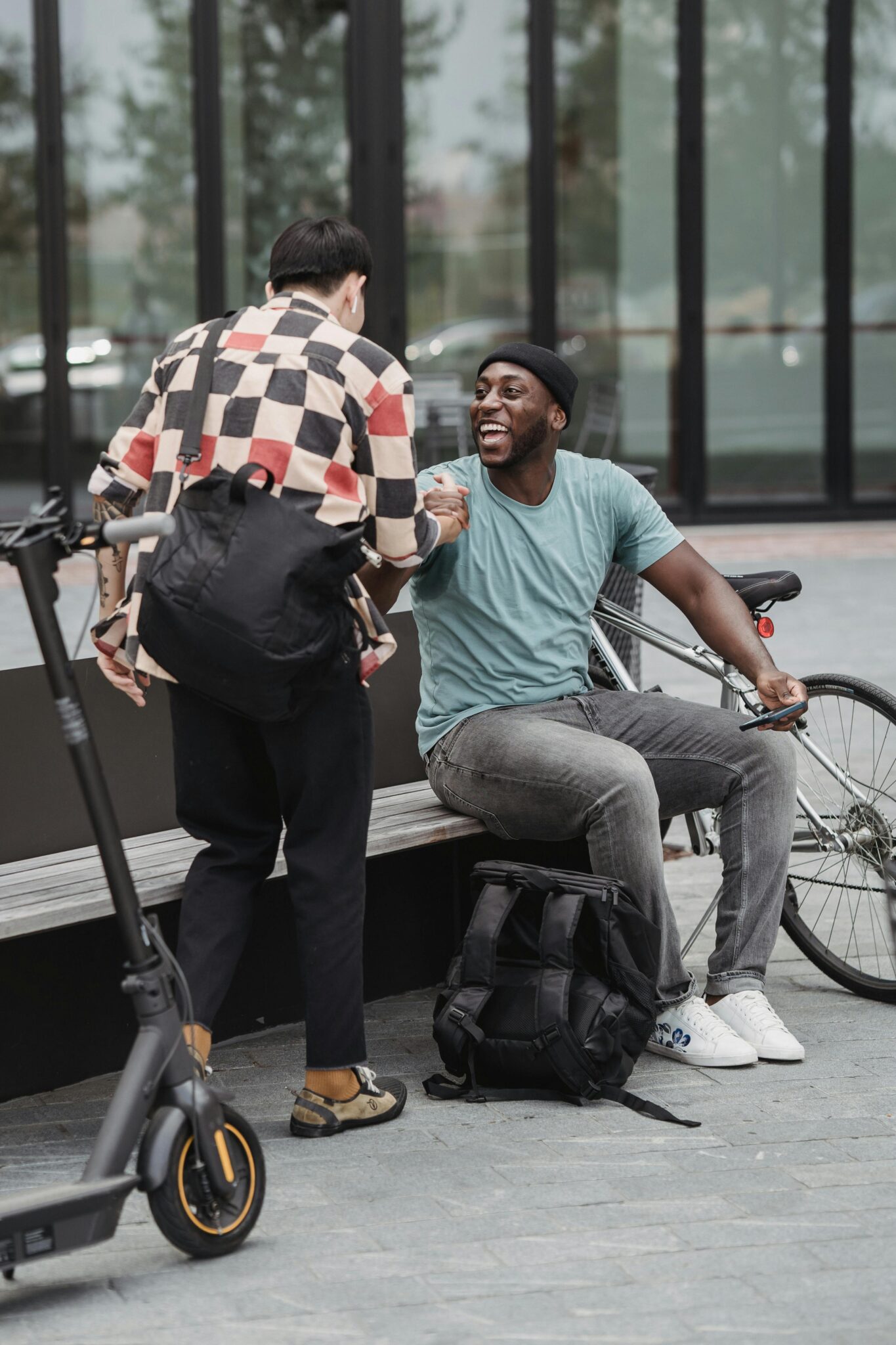 Men greeting each other with happiness, next to a bicycle and scooter in an urban setting.