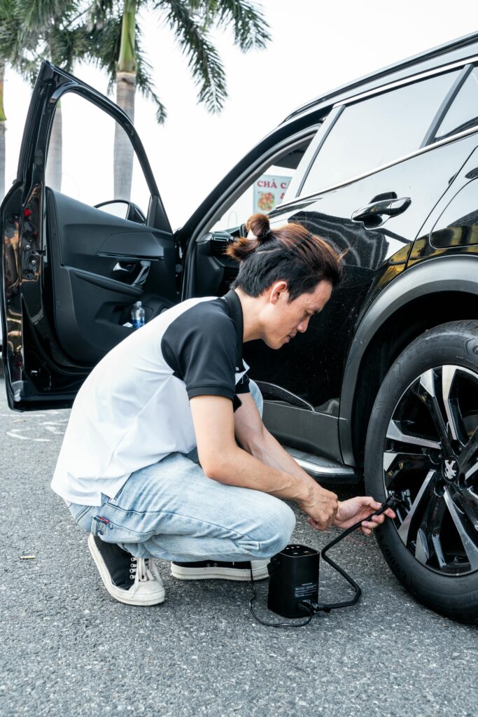 Asian man using a pump to inflate a car tire on a city street in Ho Chi Minh City, Vietnam.