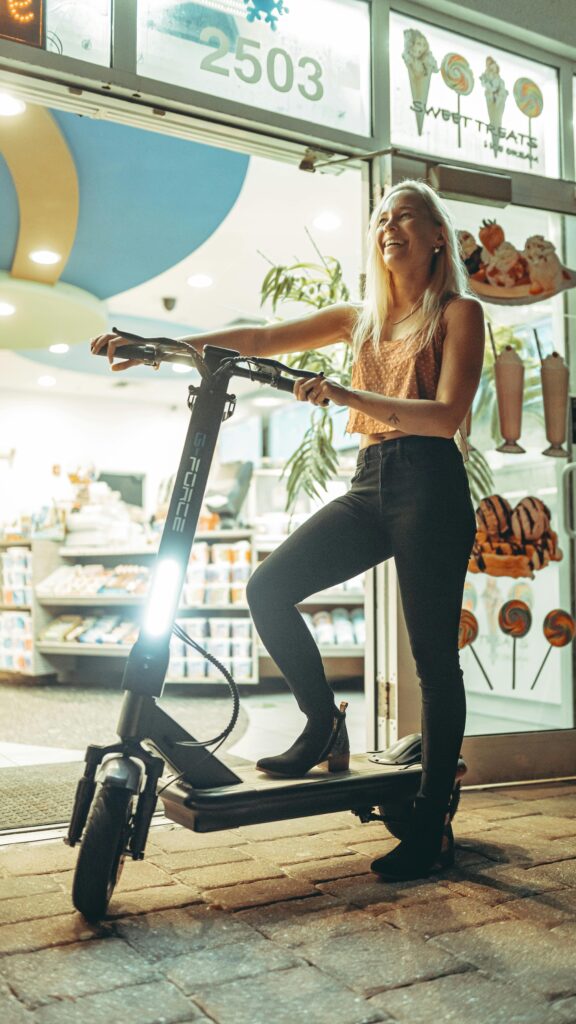 Young woman enjoys an evening urban ride on an electric scooter outside a city shop.