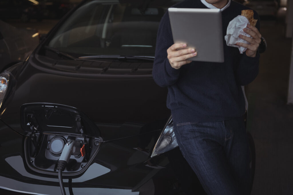 Man using digital tablet while charging electric car in garage