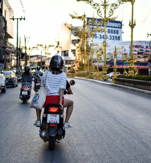 Projects 10 Motorcyclists ride through a bustling street in Chiang Rai, Thailand, showcasing urban life.