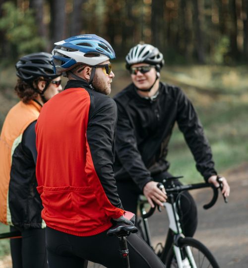 Projects 6 Three cyclists taking a break on a forest path, wearing protective gear and having a conversation.